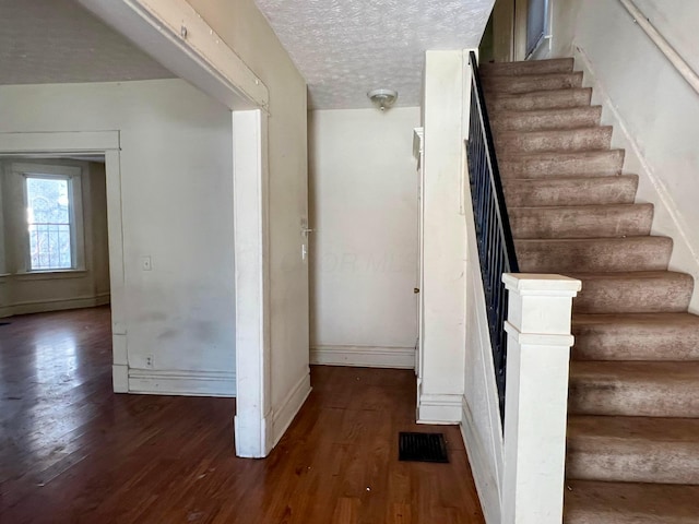 stairway with a baseboard heating unit, a textured ceiling, and hardwood / wood-style flooring