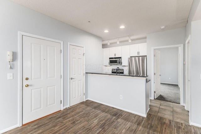 kitchen with backsplash, white cabinets, rail lighting, dark hardwood / wood-style floors, and stainless steel appliances