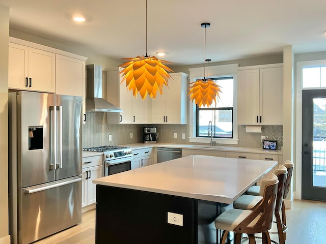 kitchen with white cabinetry, stainless steel appliances, a center island, wall chimney range hood, and sink