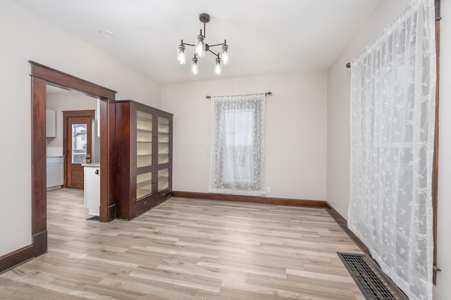 empty room with a wealth of natural light, an inviting chandelier, and light wood-type flooring