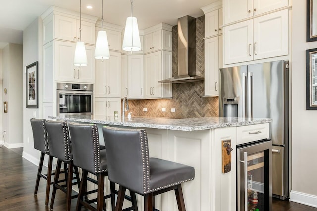 kitchen featuring wall chimney range hood, wine cooler, decorative light fixtures, white cabinetry, and stainless steel appliances