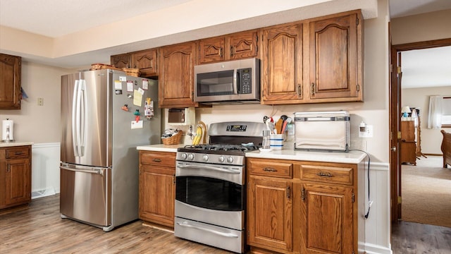 kitchen featuring light wood-type flooring, brown cabinetry, stainless steel appliances, and light countertops