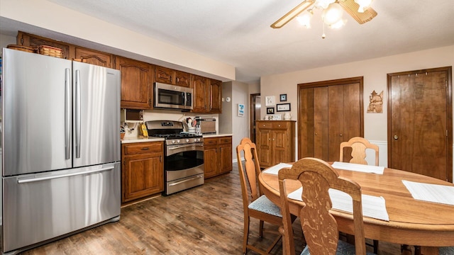 kitchen featuring brown cabinetry, a ceiling fan, dark wood-style flooring, stainless steel appliances, and light countertops