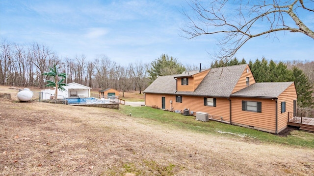 view of property exterior with roof with shingles, a lawn, crawl space, a deck, and an outdoor structure