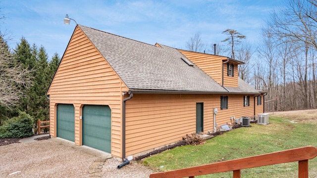 view of home's exterior featuring roof with shingles, a detached garage, central AC unit, and a lawn