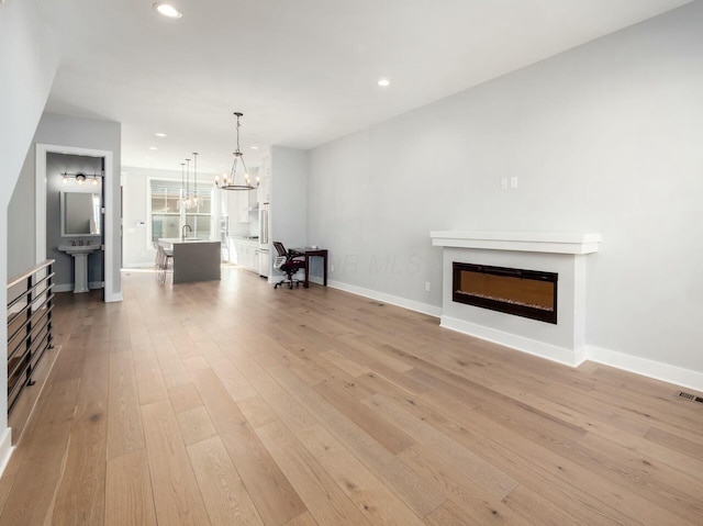 unfurnished living room featuring sink, light wood-type flooring, and a notable chandelier