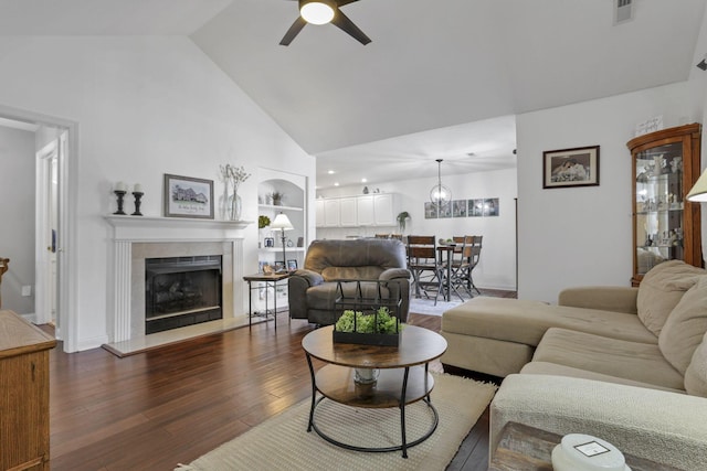 living room featuring built in shelves, dark wood-type flooring, vaulted ceiling, ceiling fan, and a fireplace