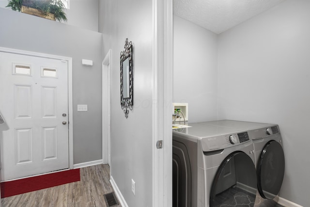 laundry area with light hardwood / wood-style flooring, a textured ceiling, and independent washer and dryer