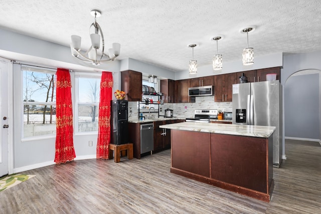 kitchen with a center island, stainless steel appliances, tasteful backsplash, pendant lighting, and dark brown cabinets