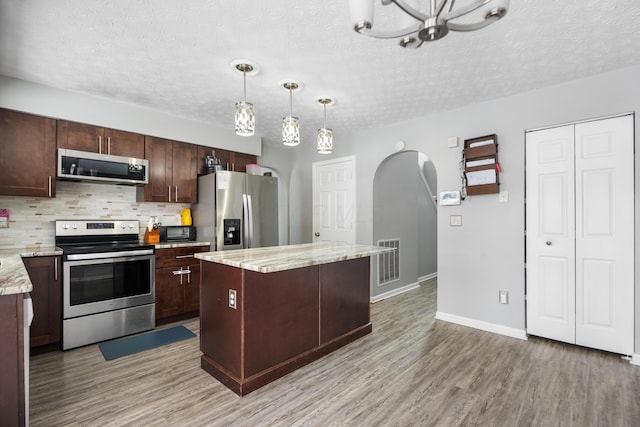 kitchen featuring light stone countertops, appliances with stainless steel finishes, tasteful backsplash, a kitchen island, and hanging light fixtures