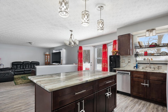 kitchen with stainless steel dishwasher, sink, pendant lighting, an inviting chandelier, and light hardwood / wood-style floors