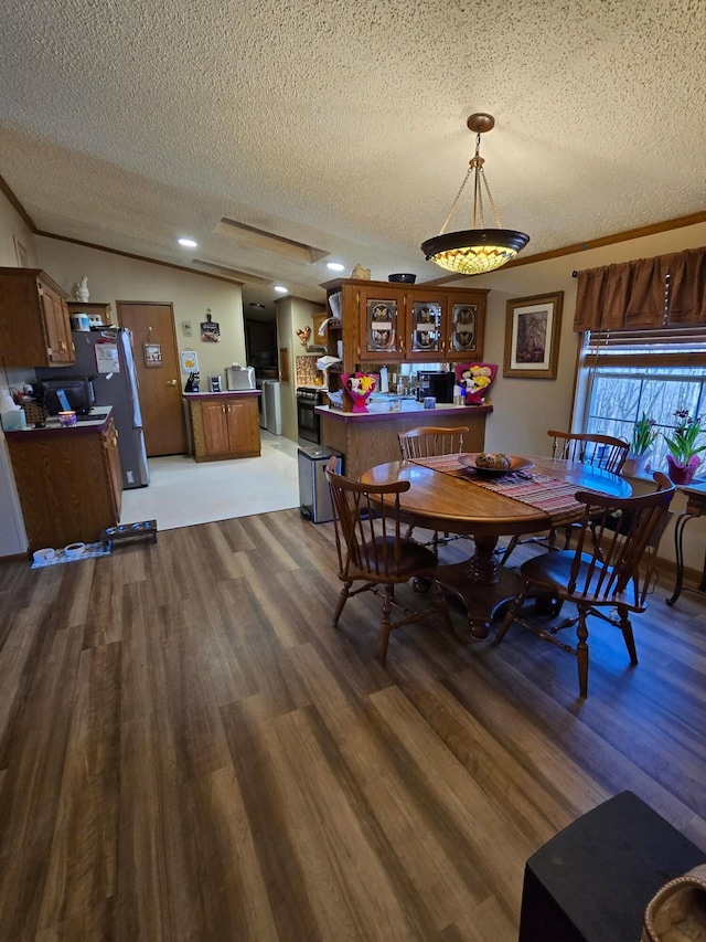 dining room with a textured ceiling, vaulted ceiling, wood finished floors, and crown molding