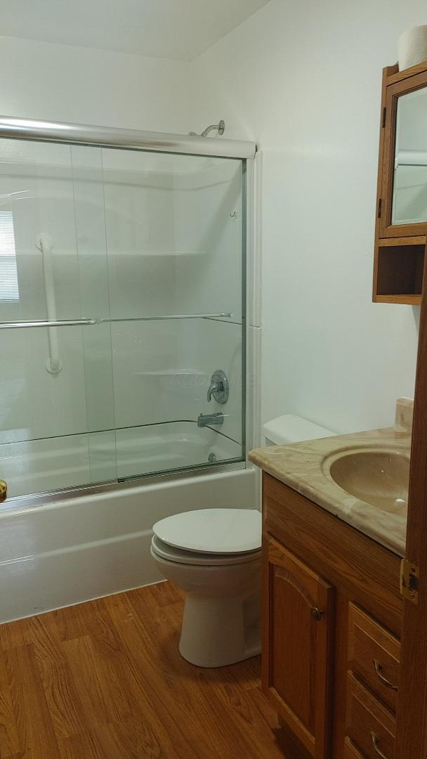 full bathroom featuring shower / bath combination with glass door, hardwood / wood-style floors, vanity, and toilet