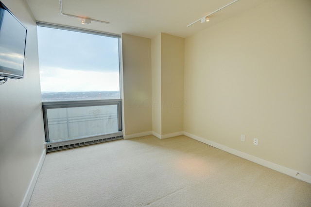 carpeted empty room featuring baseboard heating, a water view, and rail lighting