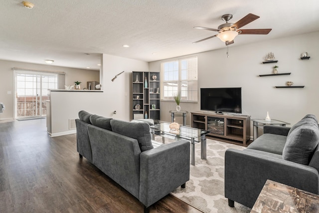 living room featuring ceiling fan, dark wood-type flooring, and a textured ceiling