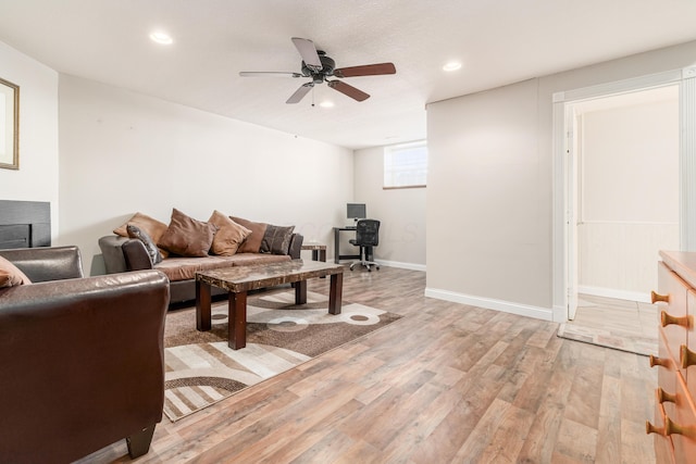 living room featuring ceiling fan, light hardwood / wood-style flooring, and a fireplace