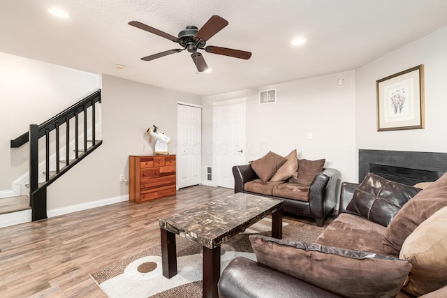 living room with ceiling fan, a textured ceiling, and light wood-type flooring