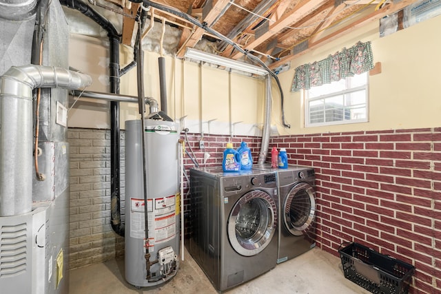 laundry room with brick wall, gas water heater, and washing machine and dryer