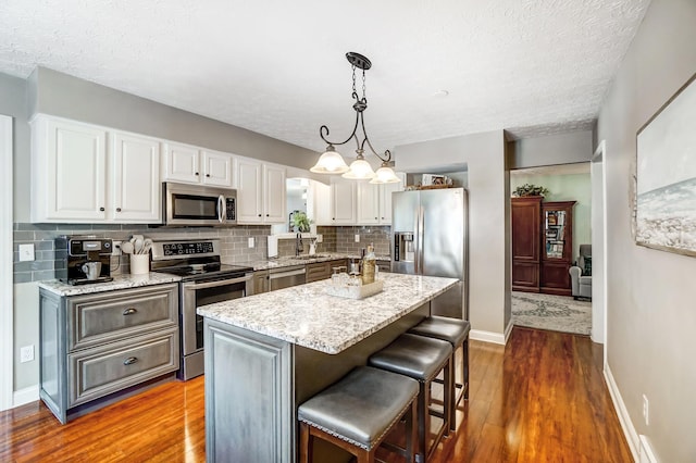 kitchen featuring dark wood-type flooring, a center island, decorative light fixtures, white cabinetry, and appliances with stainless steel finishes