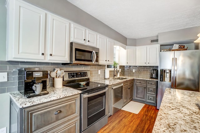 kitchen with sink, white cabinets, wood-type flooring, backsplash, and appliances with stainless steel finishes