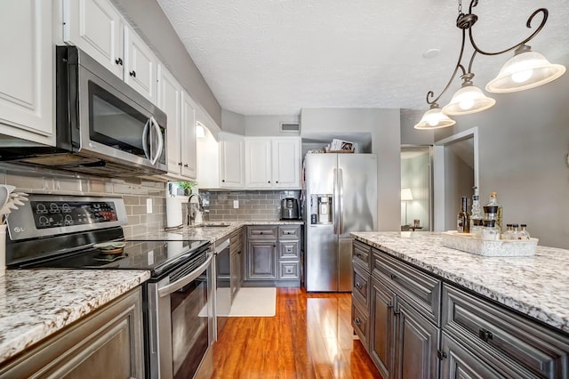 kitchen with stainless steel appliances, white cabinetry, hardwood / wood-style floors, backsplash, and hanging light fixtures