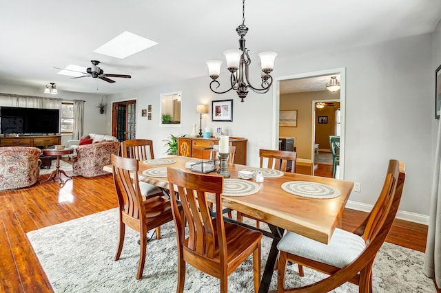 dining room with ceiling fan with notable chandelier, wood-type flooring, and a skylight