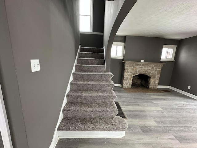 stairway with a textured ceiling, hardwood / wood-style flooring, and a stone fireplace