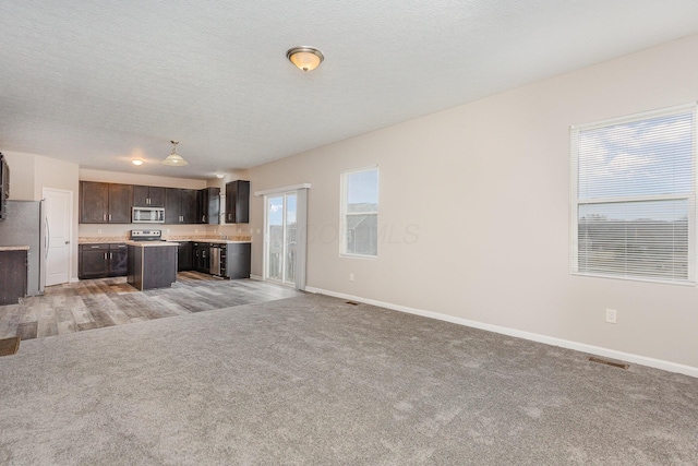 unfurnished living room with light carpet, a textured ceiling, and baseboards