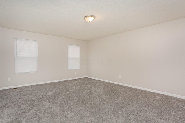 unfurnished room with a textured ceiling, carpet floors, visible vents, and baseboards