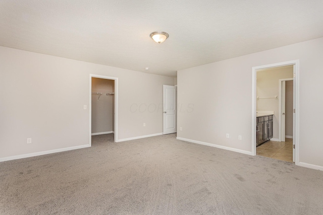 unfurnished bedroom with a walk in closet, a closet, ensuite bathroom, light carpet, and baseboards