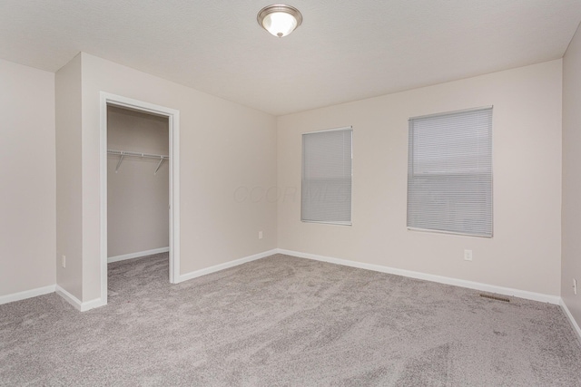 unfurnished bedroom with carpet, a spacious closet, baseboards, and a closet