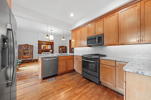 kitchen with kitchen peninsula, appliances with stainless steel finishes, backsplash, light stone counters, and pendant lighting