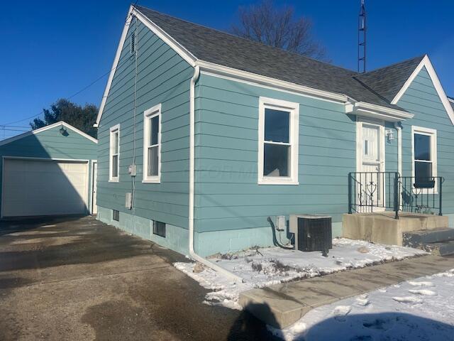 view of snow covered exterior with an outbuilding, cooling unit, and a garage