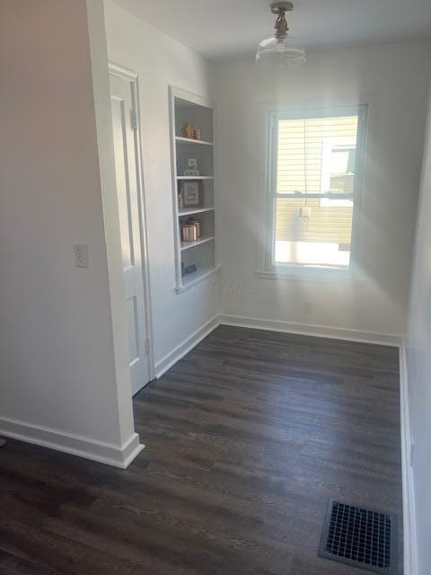 unfurnished room featuring built in features and dark hardwood / wood-style floors