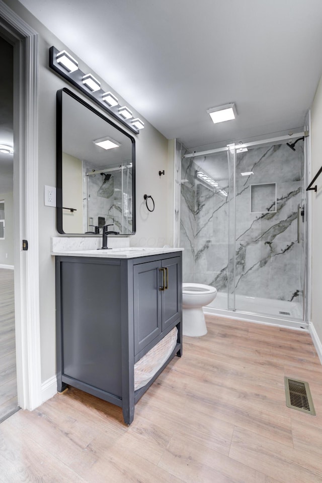 bathroom featuring wood-type flooring, vanity, toilet, and a shower with door