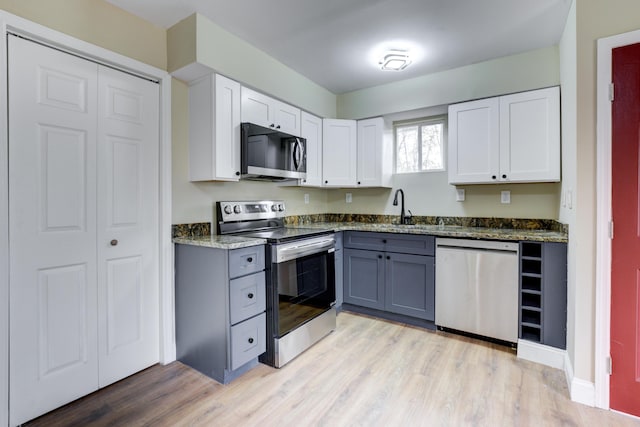 kitchen featuring appliances with stainless steel finishes, gray cabinets, white cabinetry, and dark stone countertops