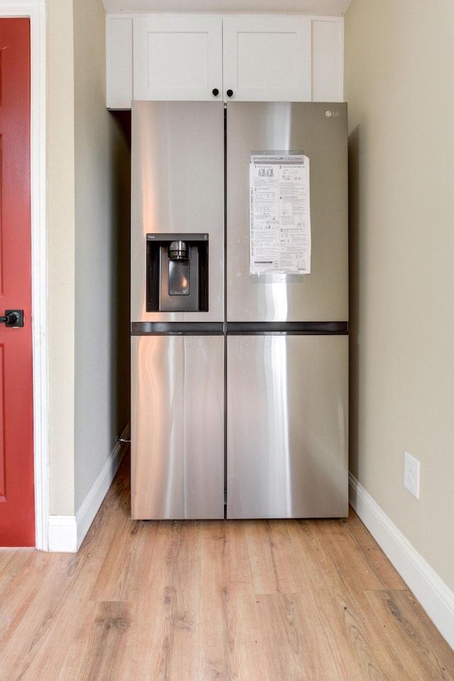 room details with white cabinetry, light hardwood / wood-style floors, and stainless steel refrigerator with ice dispenser