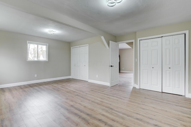 unfurnished bedroom featuring light wood-type flooring and multiple closets