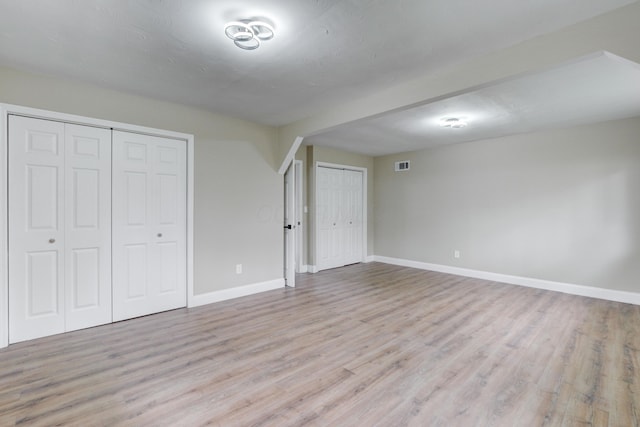 unfurnished bedroom with light wood-type flooring and multiple closets