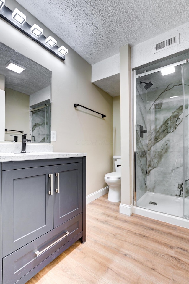 bathroom featuring walk in shower, wood-type flooring, a textured ceiling, toilet, and vanity