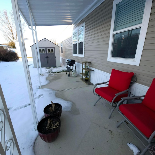 snow covered patio with grilling area and a storage shed