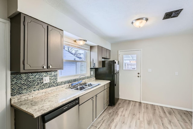 kitchen with sink, tasteful backsplash, black fridge, stainless steel dishwasher, and light hardwood / wood-style floors