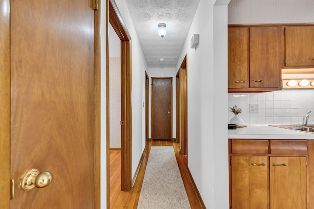 corridor with sink, light hardwood / wood-style floors, and a textured ceiling