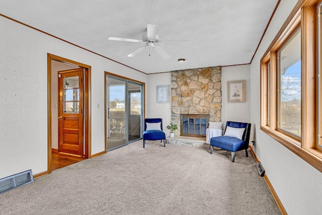 living area with a fireplace, carpet, ceiling fan, crown molding, and a textured ceiling