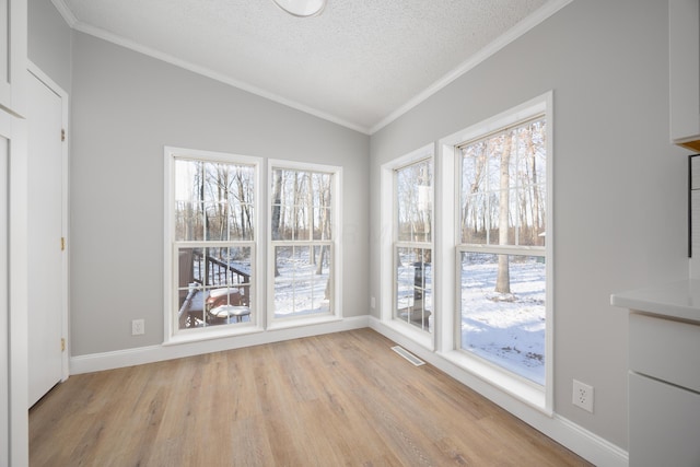 unfurnished dining area featuring crown molding, light wood-type flooring, a textured ceiling, and vaulted ceiling