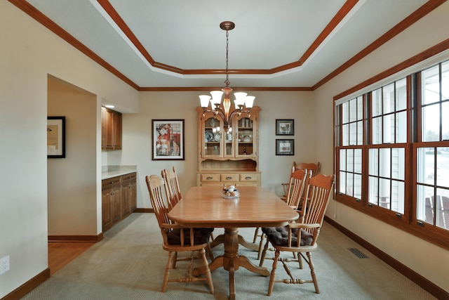 carpeted dining room with a tray ceiling, plenty of natural light, ornamental molding, and a chandelier