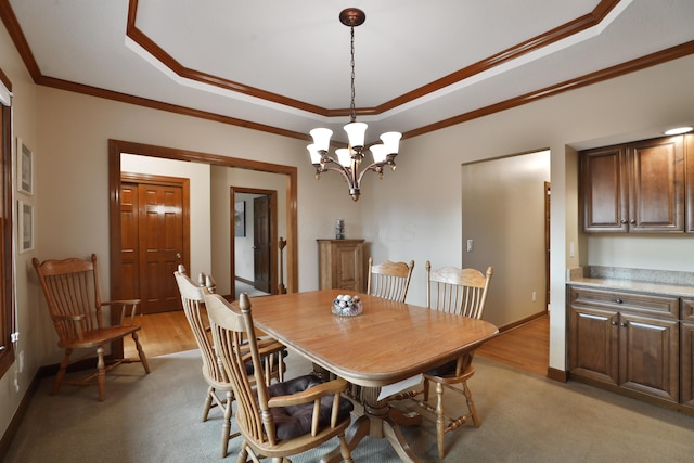 carpeted dining room with an inviting chandelier, a tray ceiling, and ornamental molding