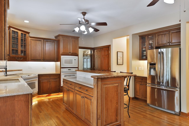 kitchen with sink, a breakfast bar area, white appliances, ceiling fan, and light hardwood / wood-style floors