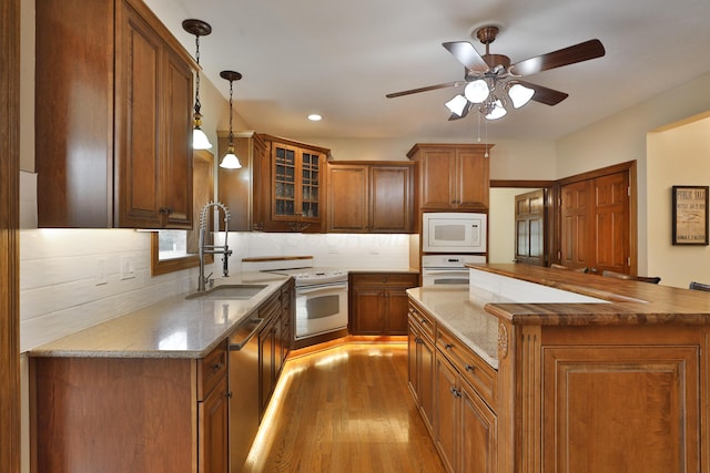 kitchen with pendant lighting, sink, light wood-type flooring, light stone counters, and white appliances