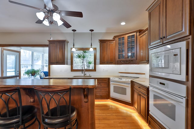 kitchen featuring decorative light fixtures, sink, backsplash, a kitchen bar, and white appliances